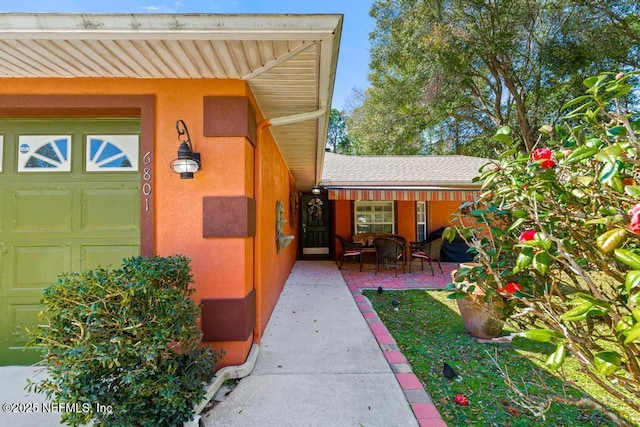 entrance to property featuring an attached garage, stucco siding, a patio area, and roof with shingles