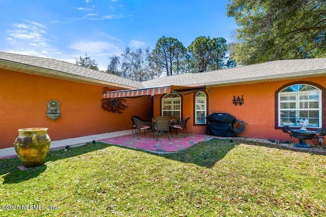 rear view of house featuring a patio area, roof with shingles, a yard, and stucco siding