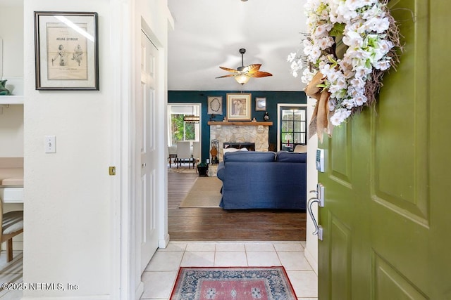 foyer with light tile patterned flooring, ceiling fan, and a stone fireplace