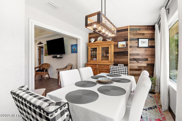 dining area with wood walls, wood finished floors, visible vents, and a notable chandelier