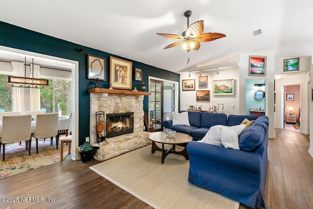 living room featuring vaulted ceiling, a stone fireplace, wood-type flooring, and visible vents