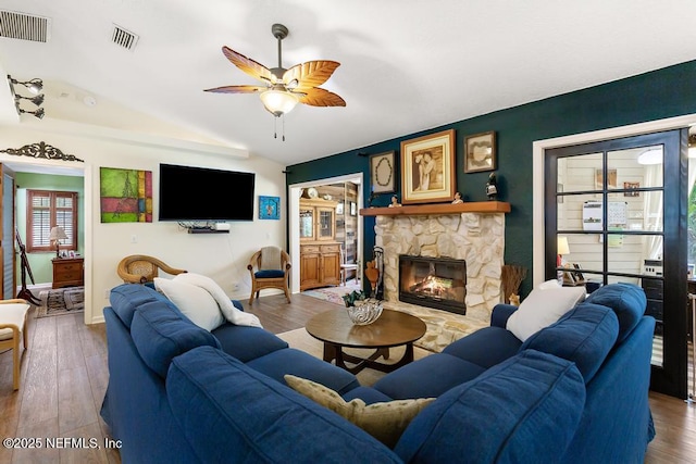 living room featuring vaulted ceiling, a stone fireplace, wood finished floors, and visible vents