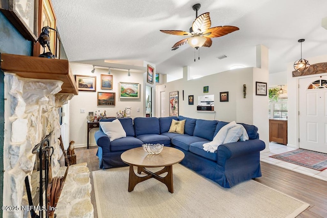 living room featuring visible vents, a ceiling fan, wood finished floors, vaulted ceiling, and a textured ceiling