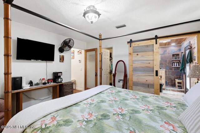 bedroom featuring a spacious closet, visible vents, a textured ceiling, and a barn door