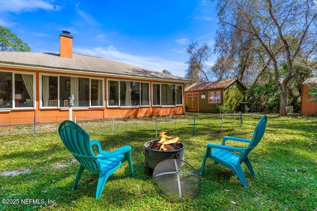 rear view of house with a fire pit, a sunroom, a yard, roof with shingles, and a chimney