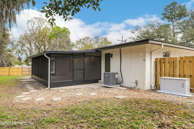 back of property featuring central air condition unit, a sunroom, fence, and stucco siding