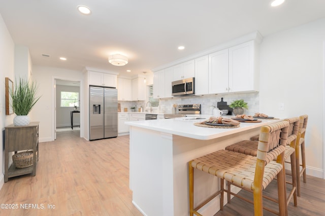 kitchen featuring appliances with stainless steel finishes, white cabinetry, a peninsula, and tasteful backsplash