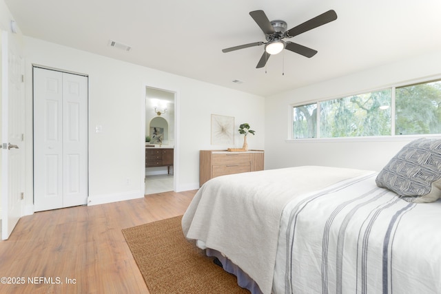 bedroom featuring light wood finished floors, baseboards, visible vents, a ceiling fan, and ensuite bath