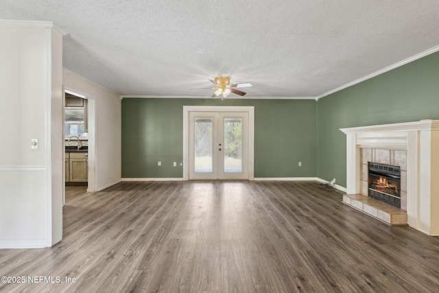 unfurnished living room with a tiled fireplace, wood finished floors, crown molding, french doors, and a sink