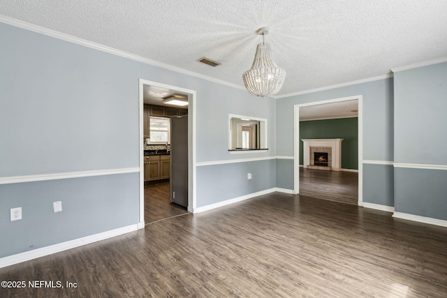 empty room with visible vents, dark wood-style floors, a textured ceiling, a fireplace, and a chandelier