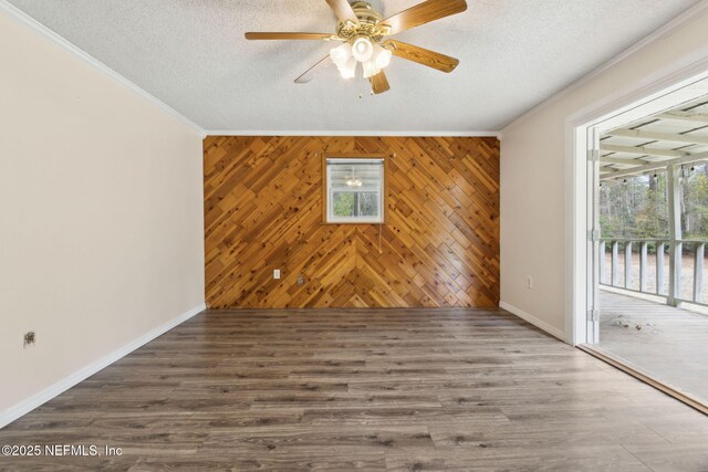 empty room with a textured ceiling, ornamental molding, wood finished floors, and baseboards