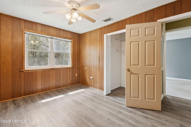 unfurnished bedroom featuring wooden walls, visible vents, a textured ceiling, light wood-style floors, and a closet