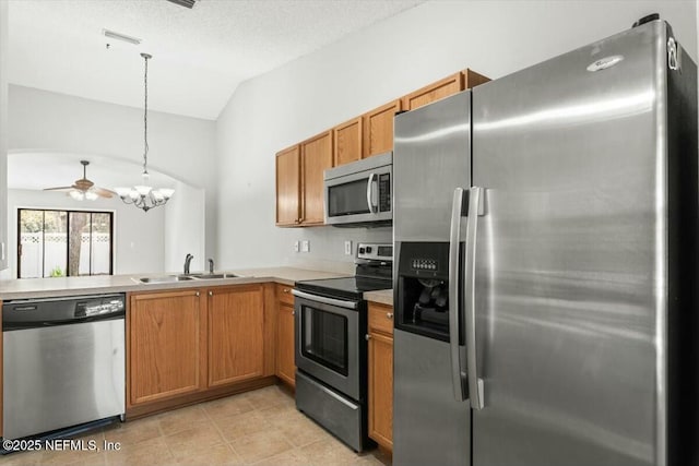 kitchen with a sink, decorative light fixtures, stainless steel appliances, brown cabinetry, and vaulted ceiling