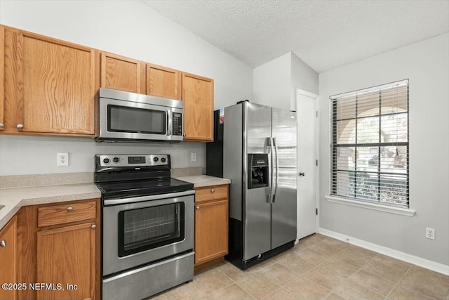 kitchen with a textured ceiling, stainless steel appliances, light countertops, baseboards, and vaulted ceiling