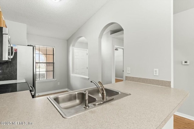 kitchen featuring electric range, a sink, light countertops, a textured ceiling, and stainless steel microwave