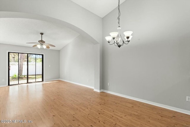 unfurnished room with light wood finished floors, baseboards, vaulted ceiling, ceiling fan with notable chandelier, and arched walkways