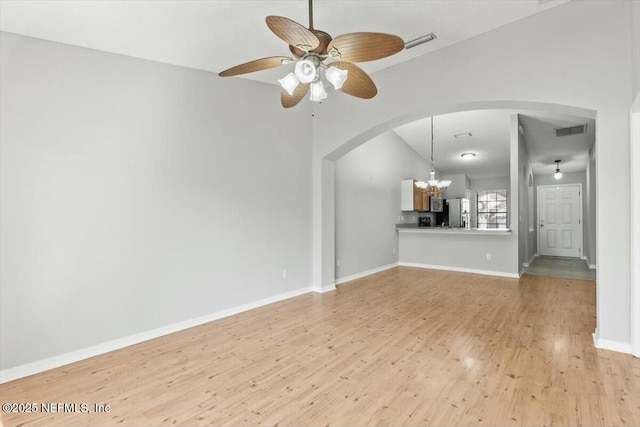 unfurnished living room featuring visible vents, baseboards, light wood-style flooring, ceiling fan with notable chandelier, and arched walkways