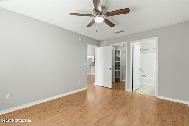 unfurnished bedroom with a spacious closet, visible vents, baseboards, light wood-type flooring, and ensuite bathroom