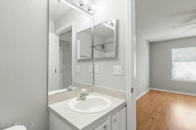 bathroom with vanity, wood finished floors, baseboards, and a textured ceiling