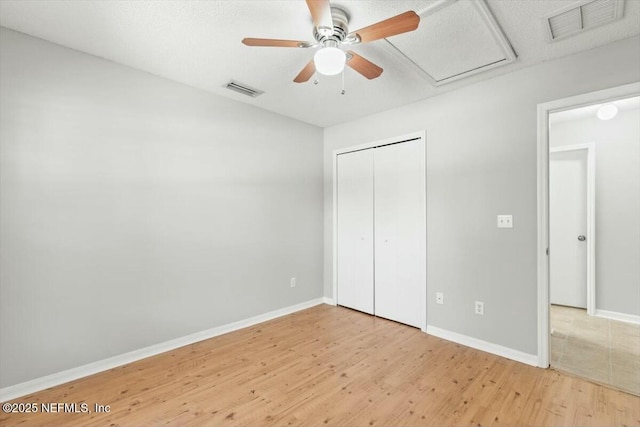 unfurnished bedroom featuring visible vents, baseboards, attic access, and wood finished floors