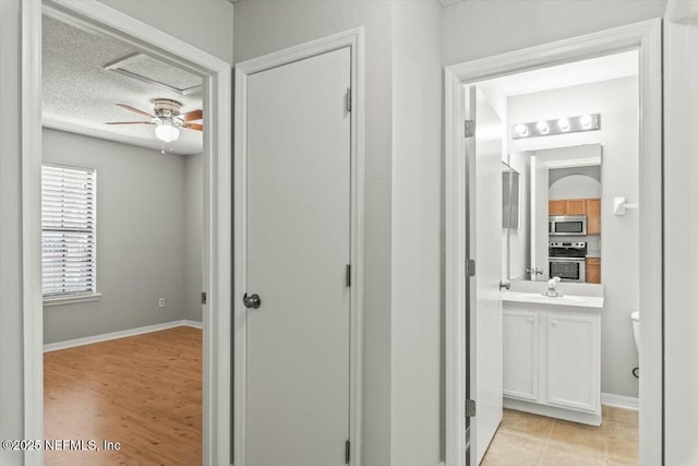 corridor featuring light tile patterned floors, a textured ceiling, and baseboards