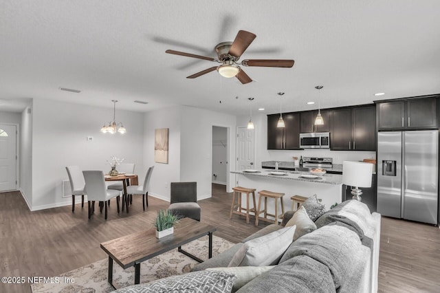 living room with visible vents, baseboards, wood finished floors, and a ceiling fan