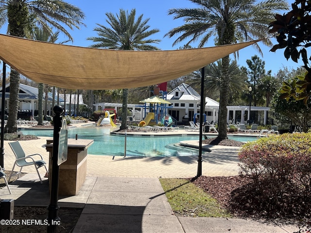 pool with playground community, a water slide, and a patio area