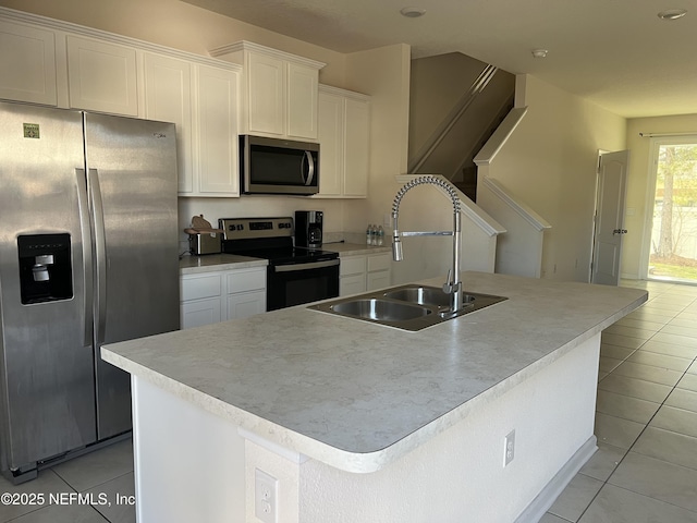 kitchen featuring light tile patterned floors, appliances with stainless steel finishes, a kitchen island with sink, white cabinets, and a sink