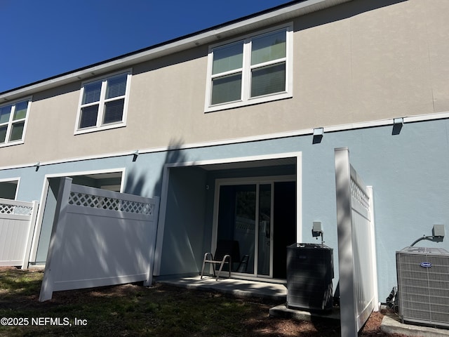 back of property featuring central AC unit, fence, and stucco siding