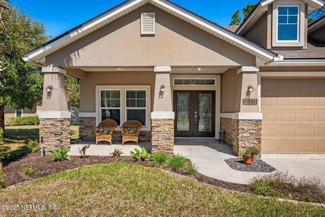 view of exterior entry with a porch, an attached garage, stucco siding, french doors, and stone siding