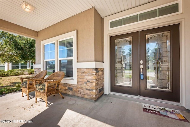 view of exterior entry with french doors, stone siding, covered porch, and stucco siding