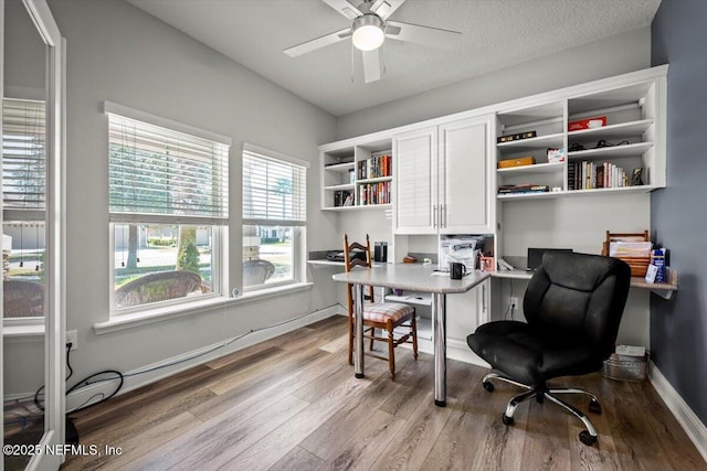 office area featuring wood finished floors, a ceiling fan, baseboards, built in study area, and a textured ceiling