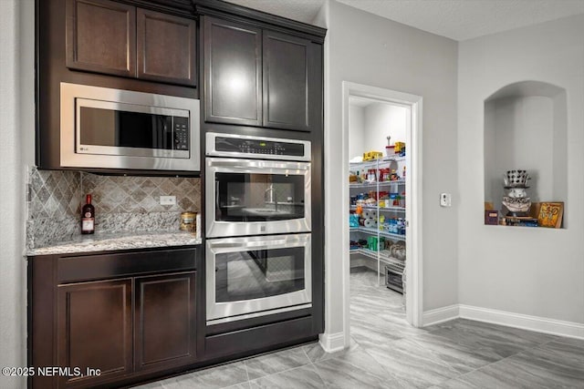 kitchen featuring tasteful backsplash, dark brown cabinets, baseboards, light stone counters, and stainless steel appliances