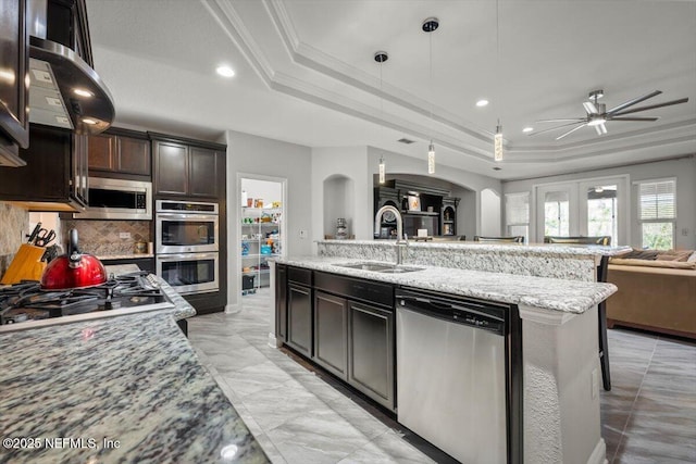 kitchen featuring open floor plan, arched walkways, stainless steel appliances, a raised ceiling, and a sink