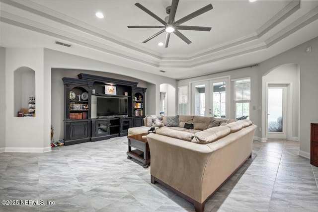 living area featuring visible vents, ornamental molding, arched walkways, a raised ceiling, and a ceiling fan