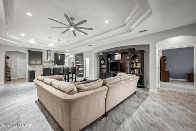 living room featuring arched walkways, a raised ceiling, ceiling fan, and ornamental molding