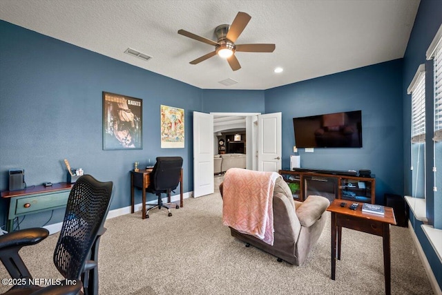 carpeted office space with visible vents, baseboards, a textured ceiling, and ceiling fan