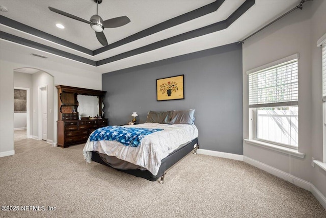 bedroom featuring a tray ceiling, arched walkways, visible vents, and carpet floors