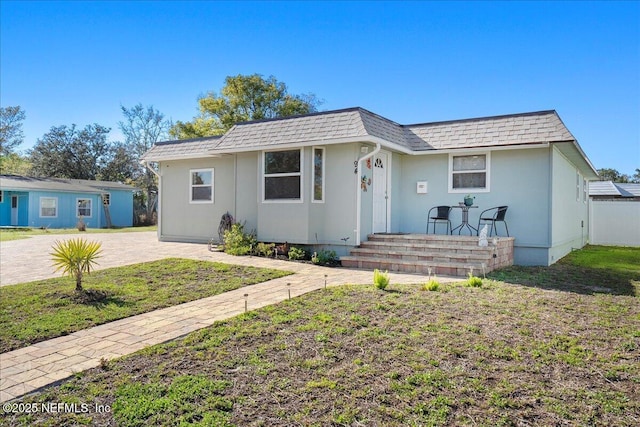 view of front of home featuring stucco siding, mansard roof, a front lawn, and roof with shingles