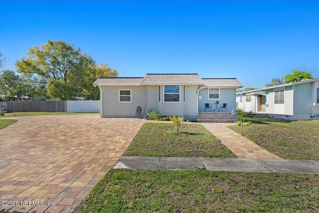 view of front of home featuring stucco siding, a shingled roof, a front lawn, and fence