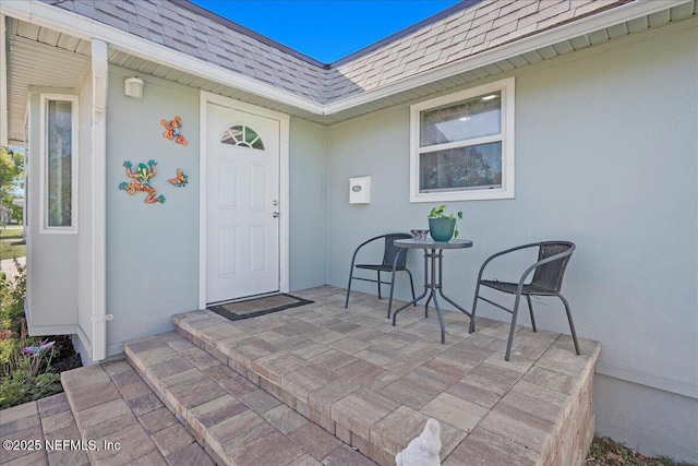 doorway to property with stucco siding, mansard roof, and roof with shingles