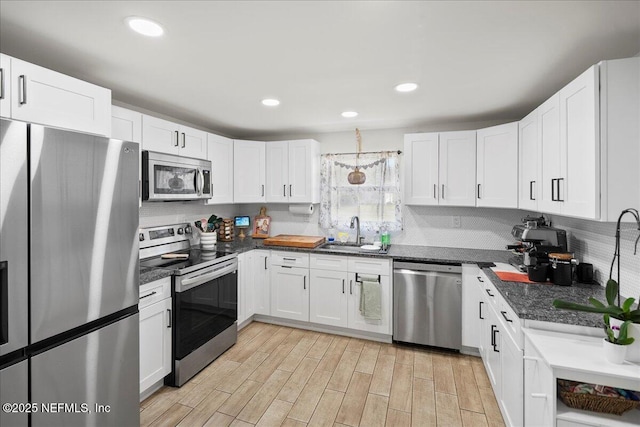 kitchen with dark countertops, stainless steel appliances, light wood-style floors, white cabinetry, and a sink