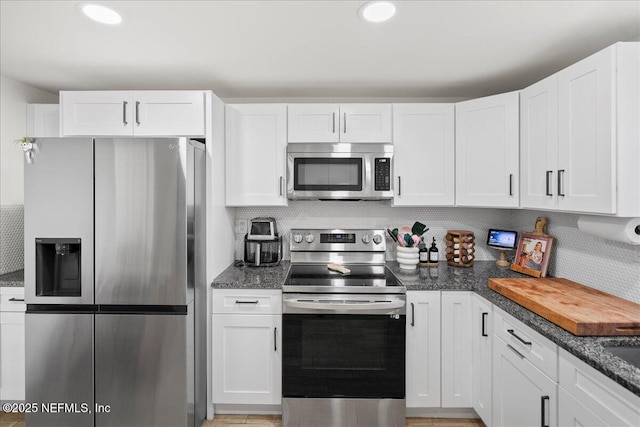 kitchen with decorative backsplash, white cabinets, stainless steel appliances, and dark stone countertops