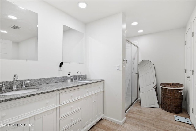 bathroom with a shower stall, wood finished floors, double vanity, and a sink