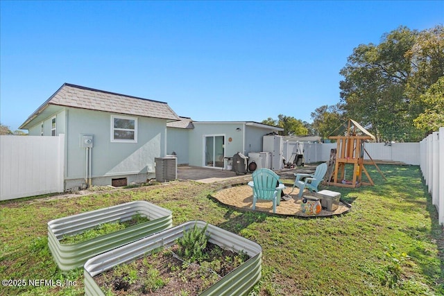 rear view of house with stucco siding, a vegetable garden, a yard, and a playground