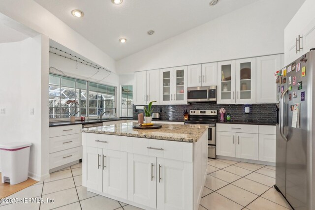 kitchen with tasteful backsplash, lofted ceiling, a center island, stainless steel appliances, and light tile patterned flooring