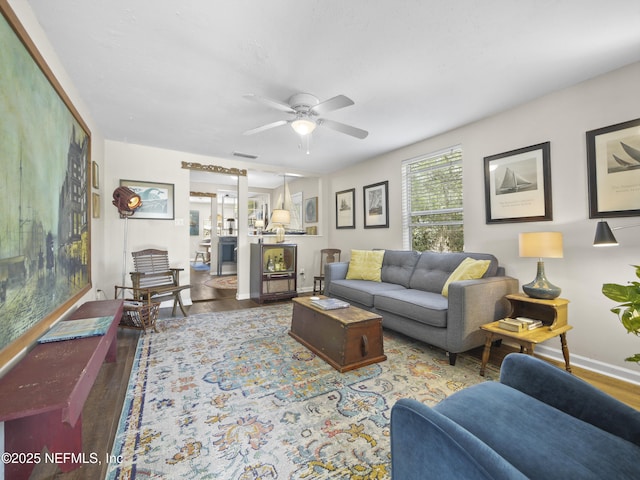 living room featuring baseboards, wood finished floors, visible vents, and a ceiling fan