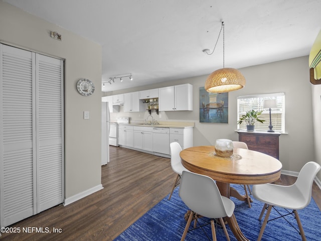 dining space with baseboards, dark wood finished floors, and track lighting