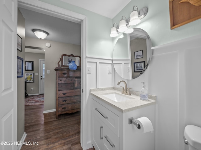 half bathroom featuring toilet, wood finished floors, vanity, and baseboards