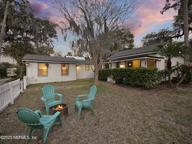 back of property featuring roof mounted solar panels, fence, a fire pit, and a yard